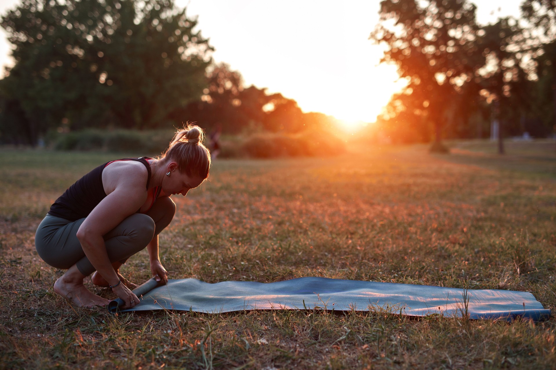 Woman folding and unfolding yoga mat in the park during sunset sunrise time.